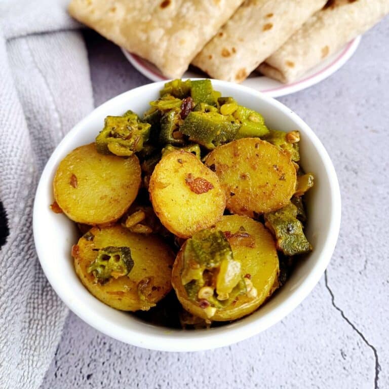 bowl of aloo bhindi curry placed on a tile with a napkin next to it.