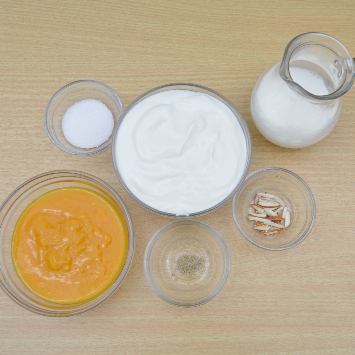 yogurt, milk, sugar, cardamom, almonds and mango pulp placed on a wooden table.