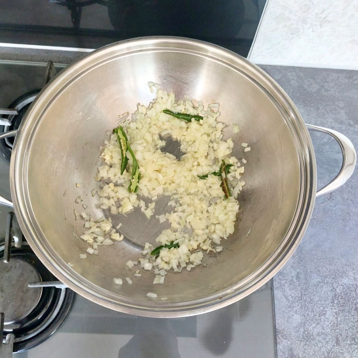 sauteing onion and green chillies in a steel pan. 