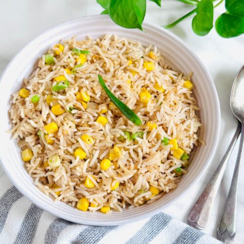 white bowl of sweetcorn fried rice placed on marble along with spoons and napkin.