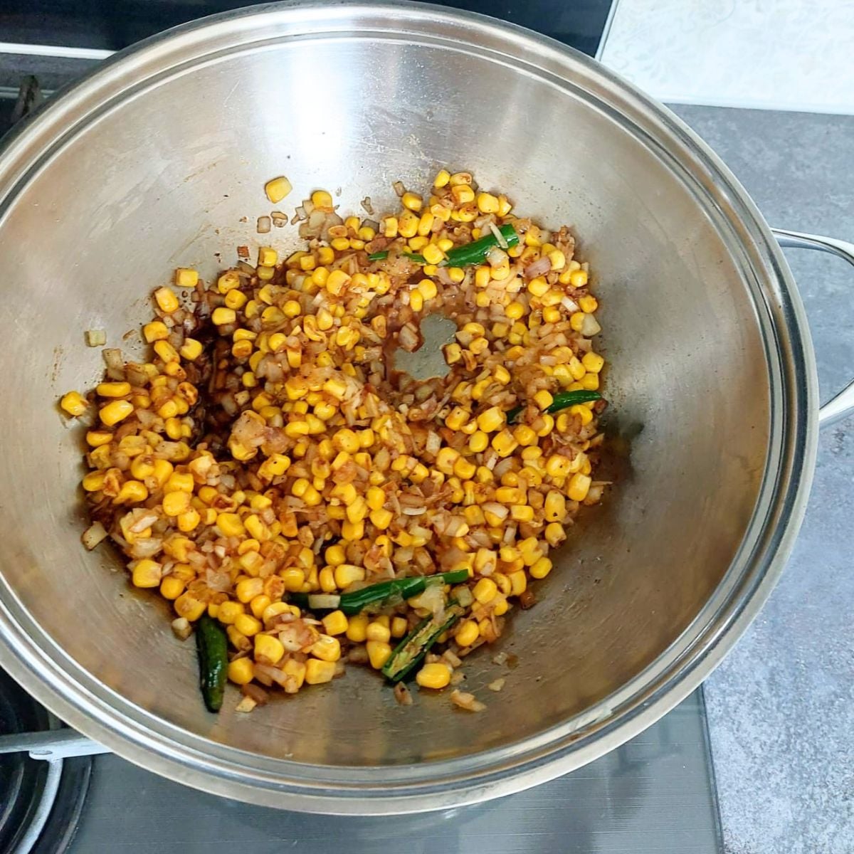 cooking sweetcorn kernels, sauces, spices and other vegetables in a steel pan