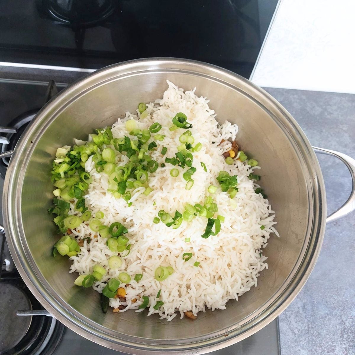 tossing rice and spring onion with cooked sweetcorn and seasonings in a steel pan.