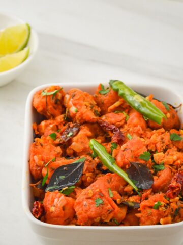 white bowl of potato 65 placed on marble along with a bowl of lemon wedges and onion slices.
