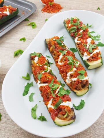 vegetarian stuffed zucchini boats placed on a white plate on a wooden table.