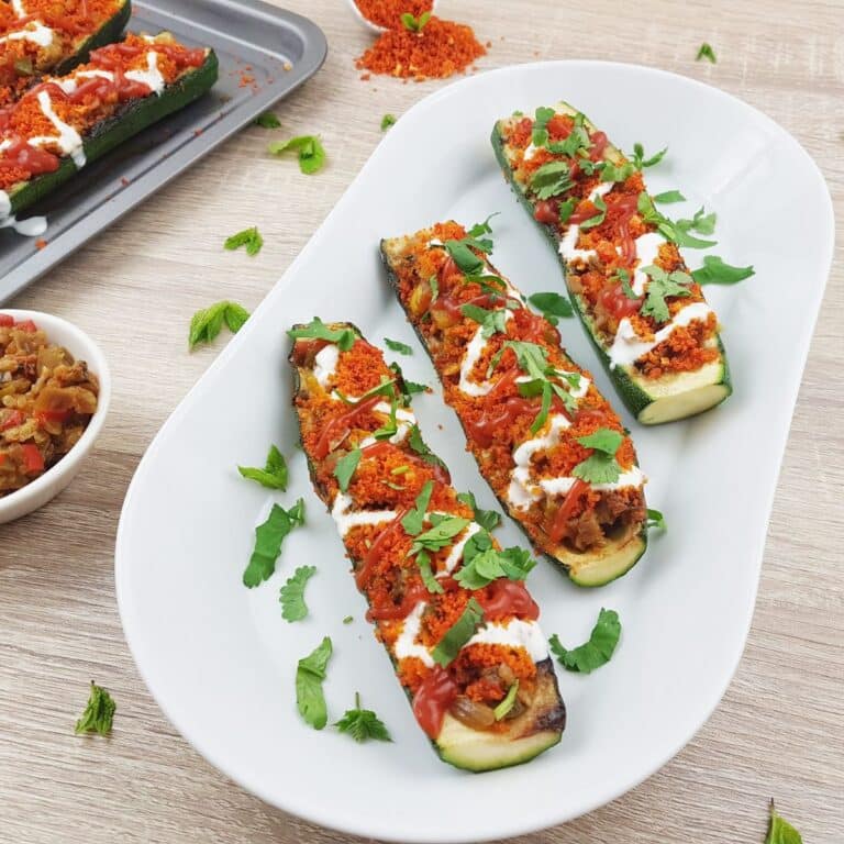 vegetarian stuffed zucchini boats placed on a white plate on a wooden table.