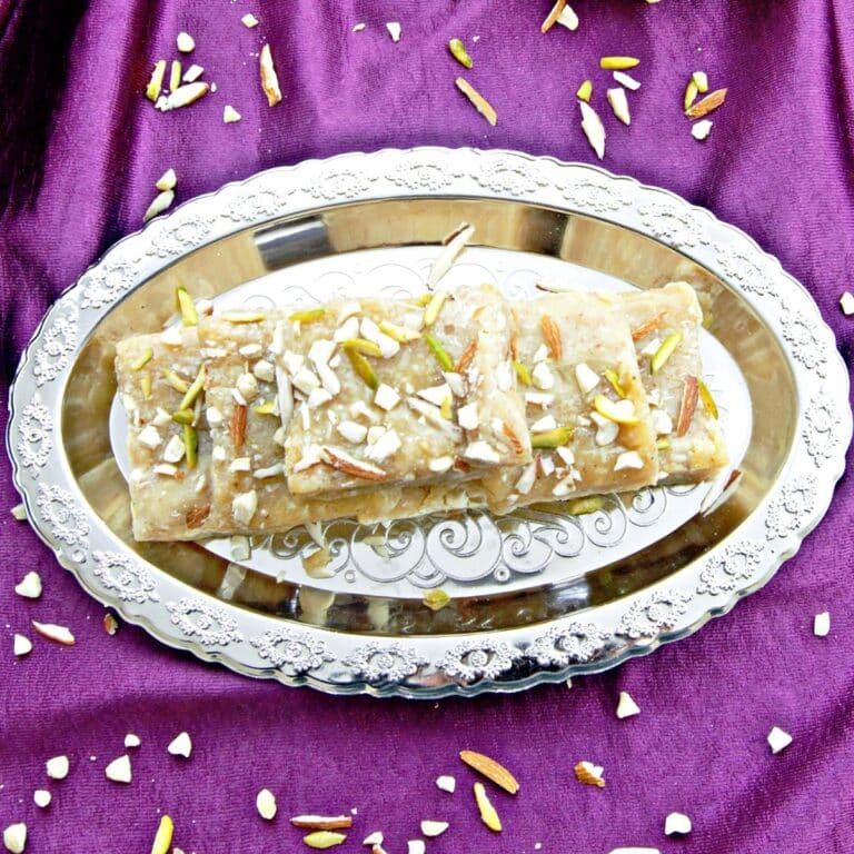 a silver plate of 7 cup burfis placed on a purple cloth.