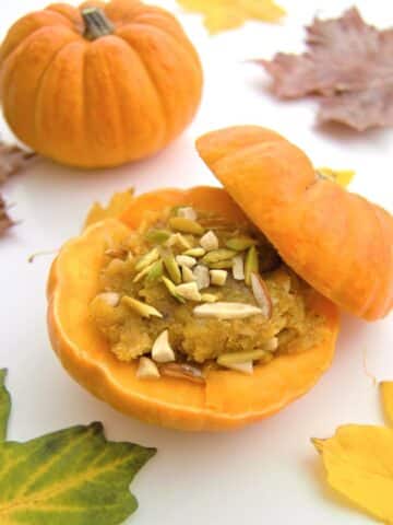 kaddu halwa inside pumpkin placed on a table along with fall leaves.