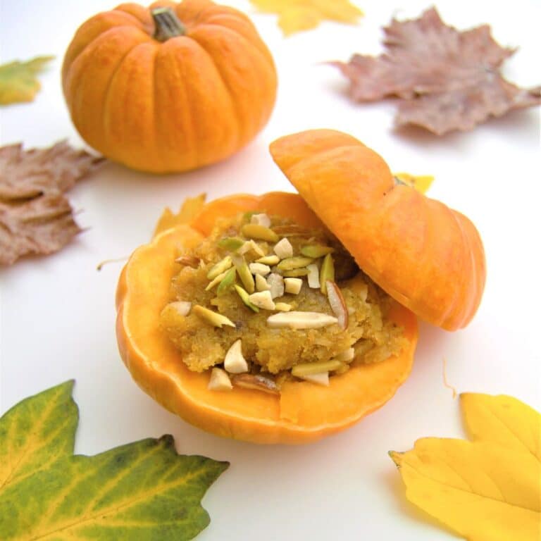 kaddu halwa inside pumpkin placed on a table along with fall leaves.