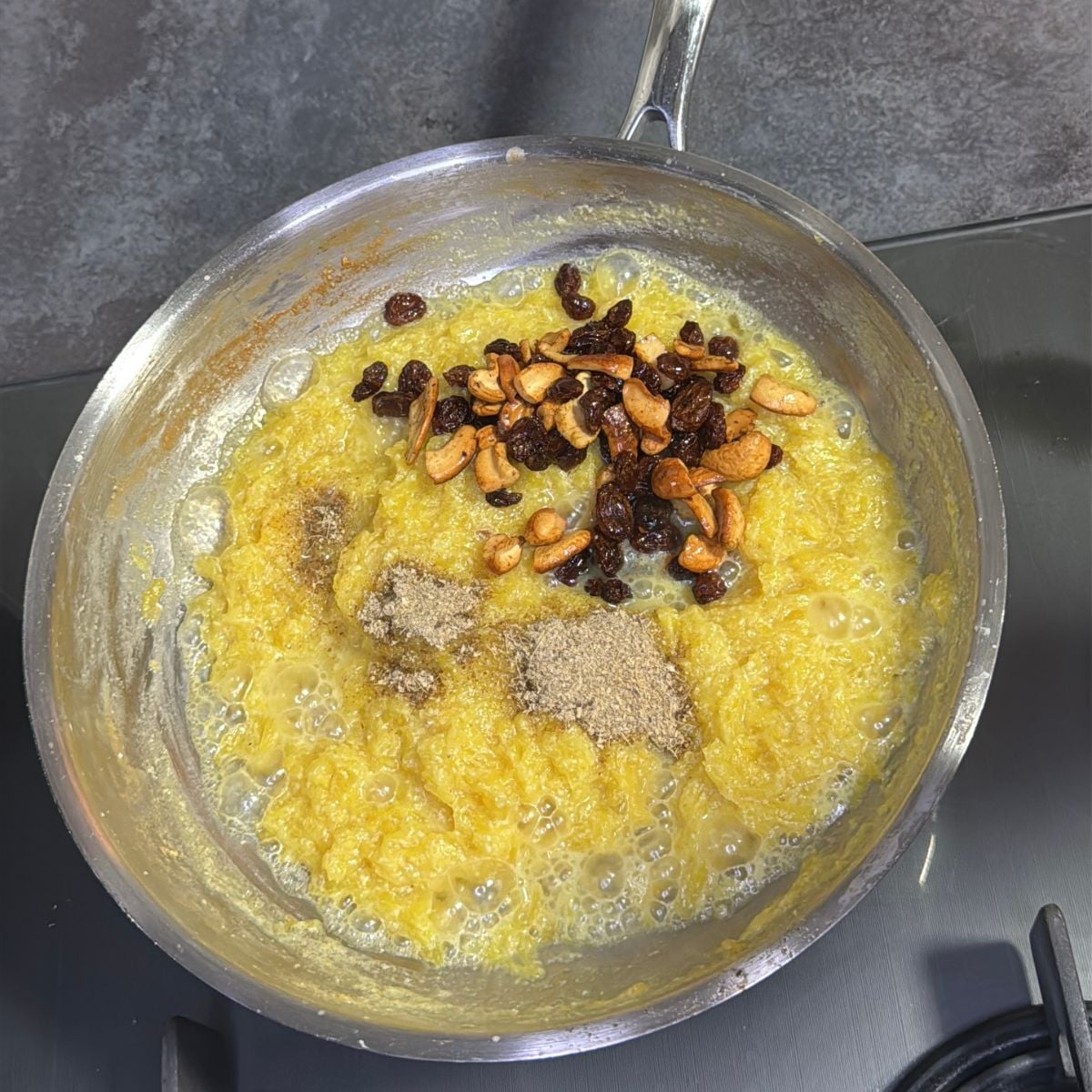 kaddu halwa in a steel pan topped with dried fruits placed on stovetop.