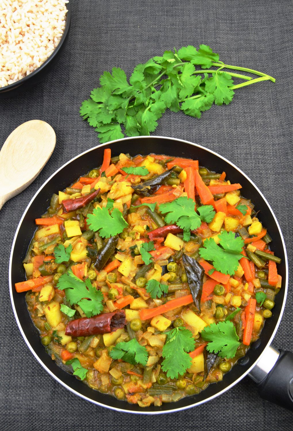 veg curry in a pan with coriander leaves rice in a bowl