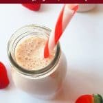 milkshake in a glass bottle with 3 strawberries in white table.
