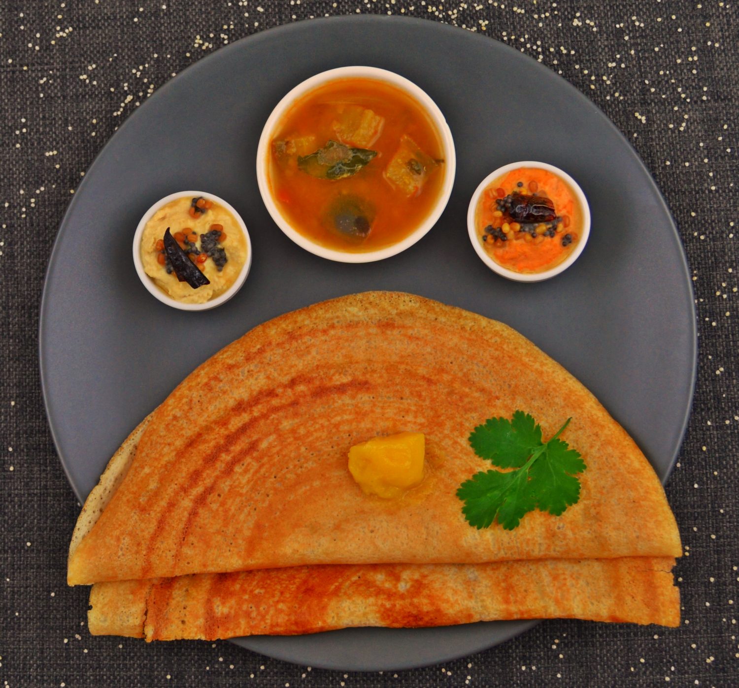 2 millet dosas sambar and 2 chutneys on black plate