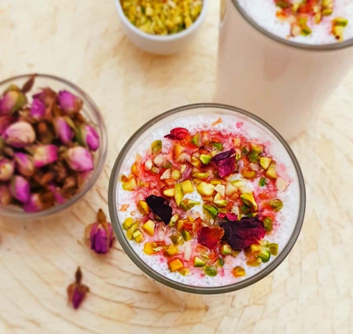 rose lassi in a glass with pistachios and rose petals as topping on wood colour placemat