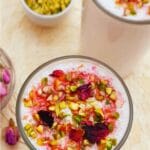 pin image of rose lassi topped with nuts and dried rose petals with text overlay on top and bottom.