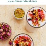 pin image of rose lassi in 2 glasses with nuts and rose petals with a blue text overlay on top.