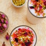 pin image of rose lassi in 2 glasses with nuts and rose petals with a text overlay on top.