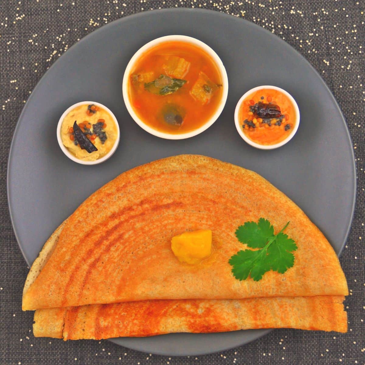 mixed millet dosa on a black plate along with chutneys and sambar.