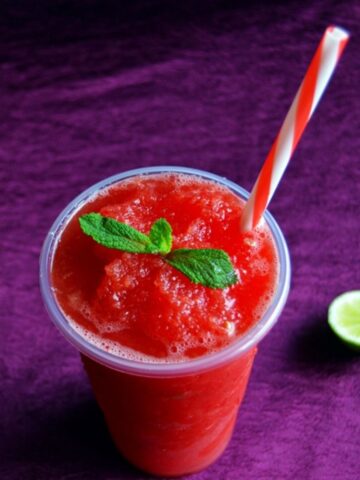 watermelon slushie in a glass topped with a mint sprig and a lime slice placed next to it.