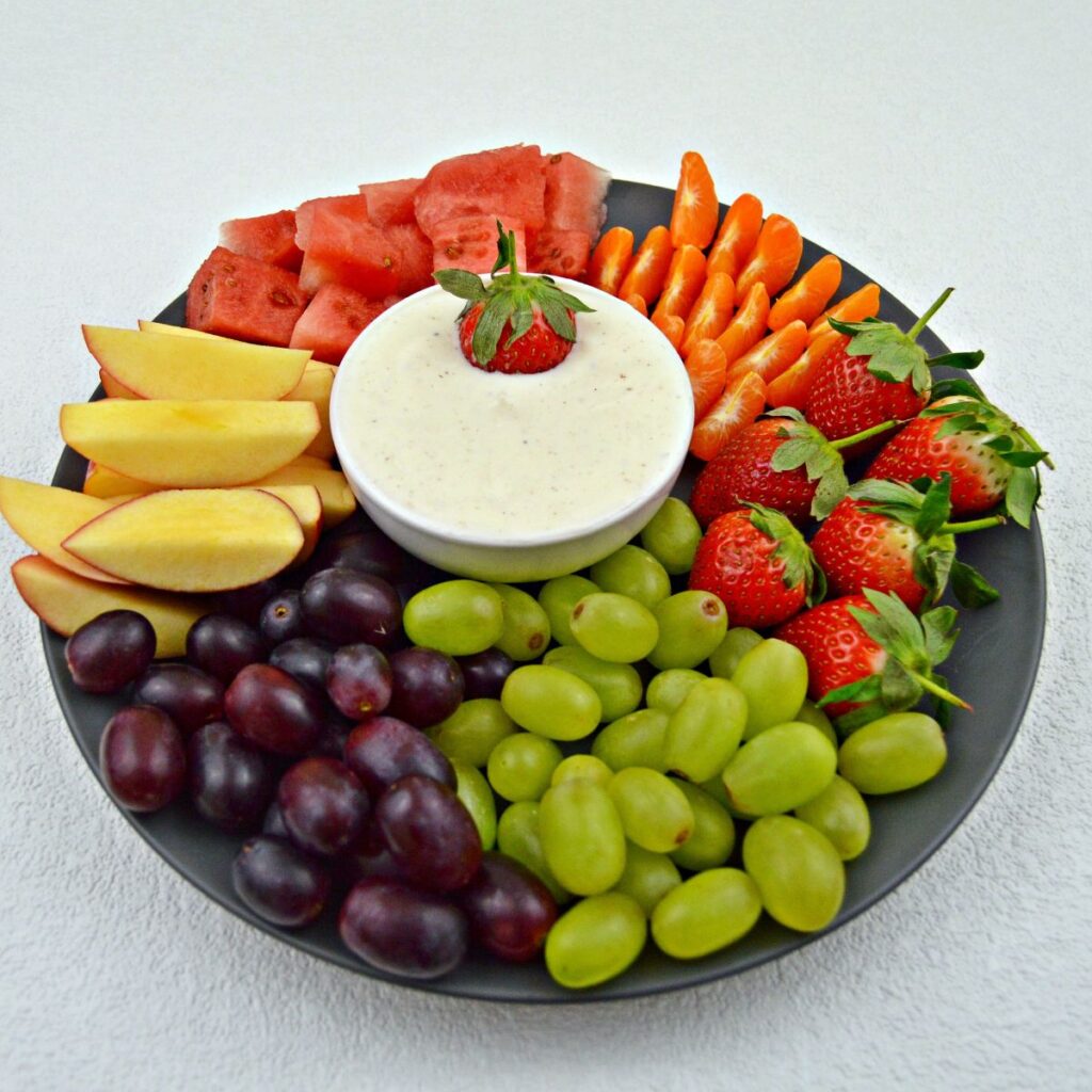 a little hand dipping strawberry in a bowl of fruit yogurt dip placed in a fruit platter.