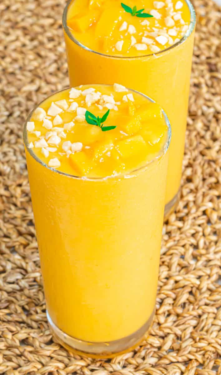 banana pineapple mango smoothie in a glass topped with nuts placed on a mat.