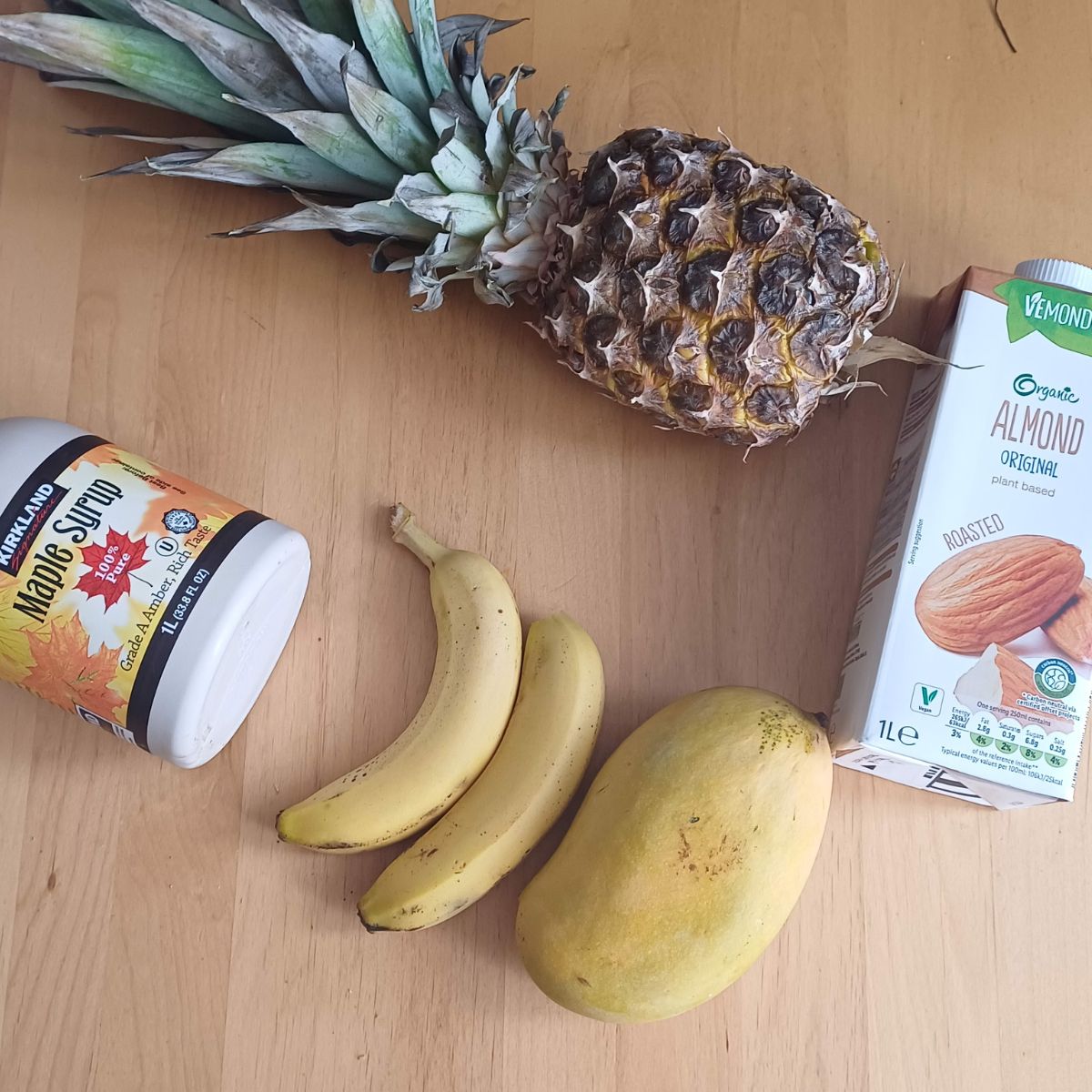 pineapple, banana, mango, almond milk and maple syrup placed on wooden table.