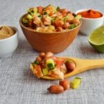 peanut chaat in a wooden spoon and in a bowl on a cloth with half cut lime, spice mix in a bowl.