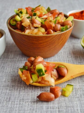 peanut chaat in a wooden spoon and in a bowl on a cloth with half cut lime, spice mix in a bowl.