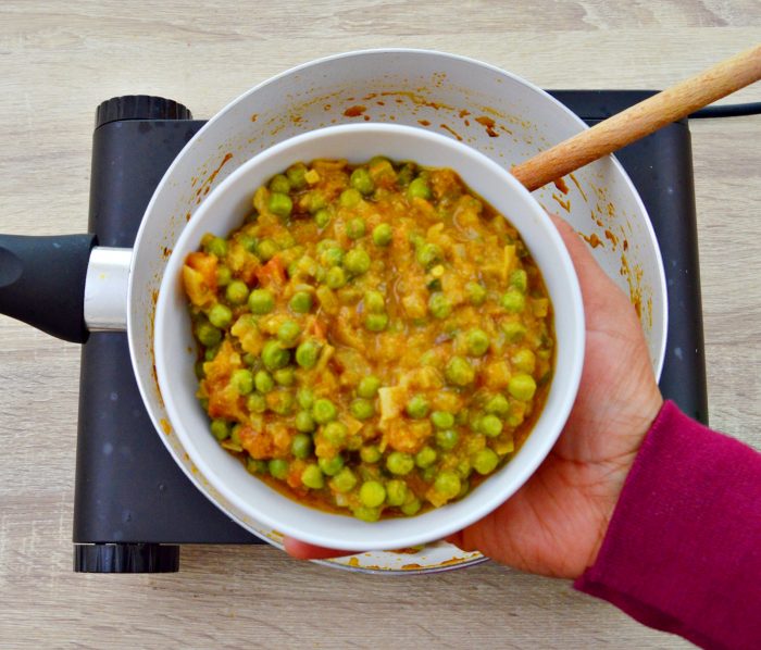 holding a bowl of green peas curry in a hand.