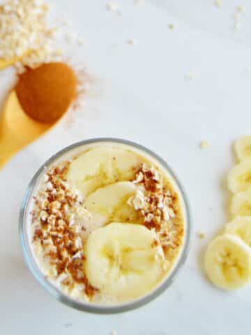 top shot of banana oatmeal smoothie in a glass with sliced bananas and oats as toppings.