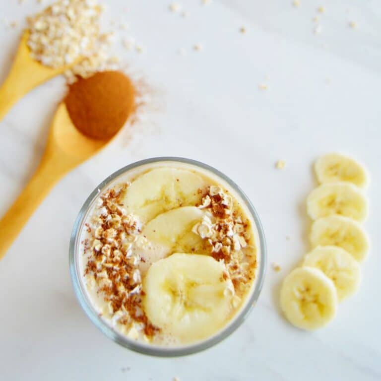 top shot of banana oatmeal smoothie in a glass with sliced bananas and oats as toppings.