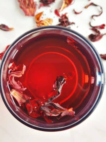 hibiscus tea in a glass placed on a marble along with dried petals.