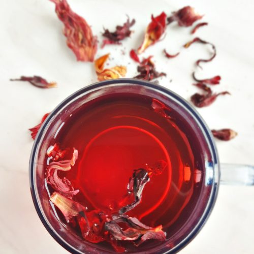 hibiscus tea in a glass with dried petals placed next to it on a marble.