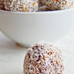 pin image of coconut date balls in a white bowl behind and one ball on a marble with text overlay on top and bottom.