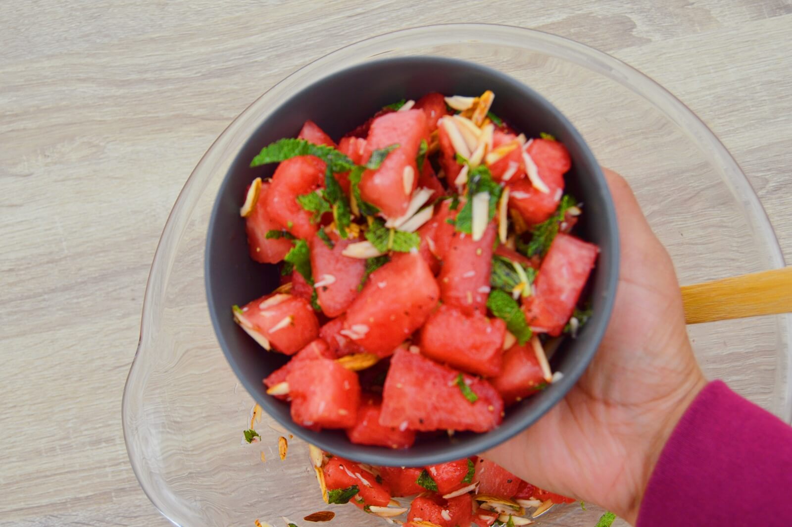 holding watermelon salad in a black bowl.