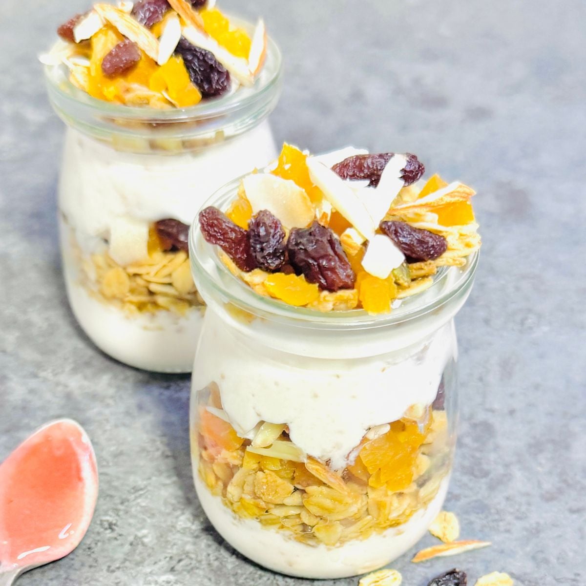 top view of two jars of strawberry yogurt granola parfait placed on a granite with a spoon of strawberry honey next to them.