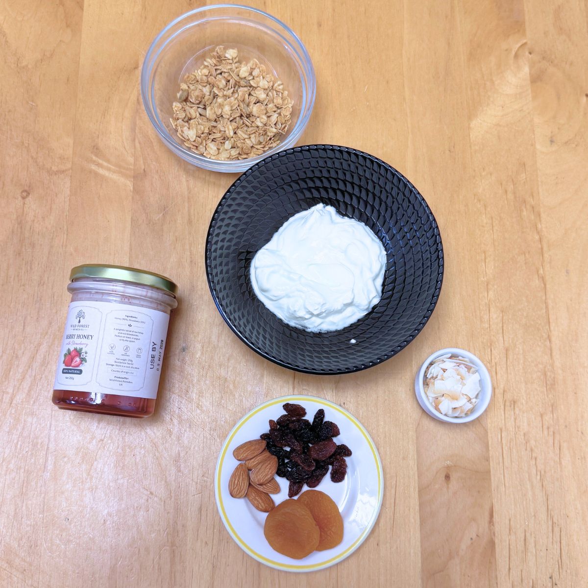 ingredients to make strawberry honey yogurt granola parfait for kids placed on wooden table.
