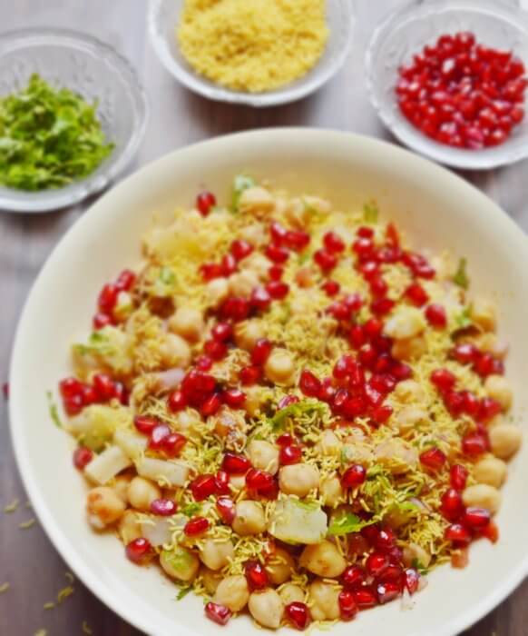 chana chaat in a bowl with coriander, sev and pomegranate in small bowls.