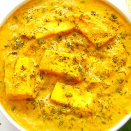 close up shot of methi malai paneer curry in a white bowl.