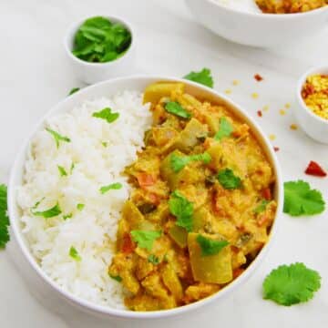 capsicum curry in a white bowl along with rice placed on a white capsicummarble.