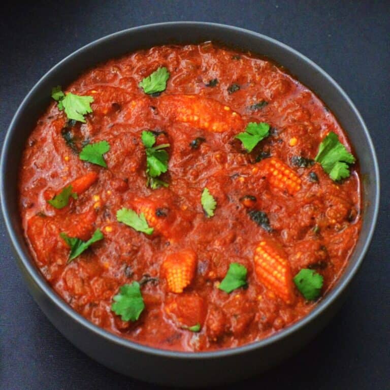 close up shot of black bowl of baby corn curry with coriander leaves garnished on top.