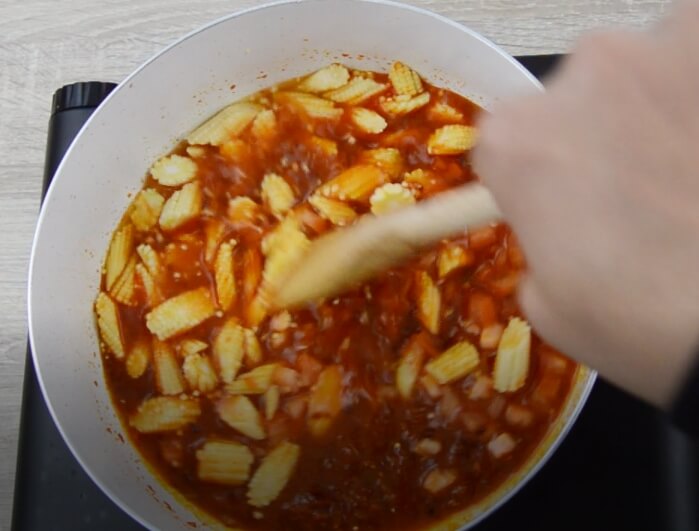 cooking baby corn with liquid and spices in a pan.