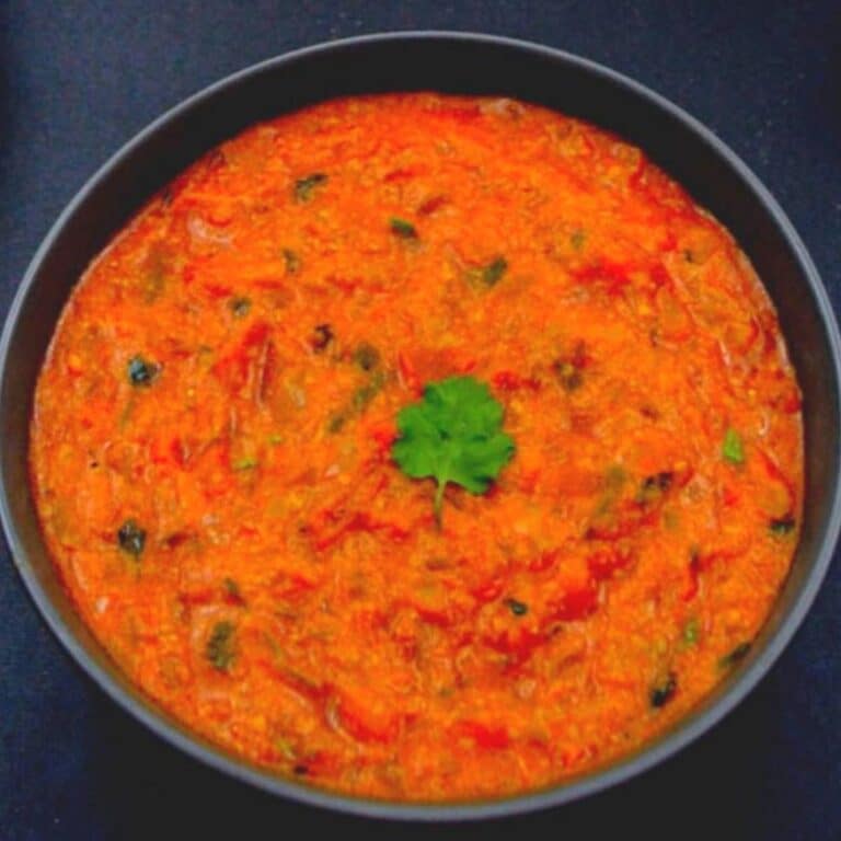 tomato kurma in black bowl placed on a black table.