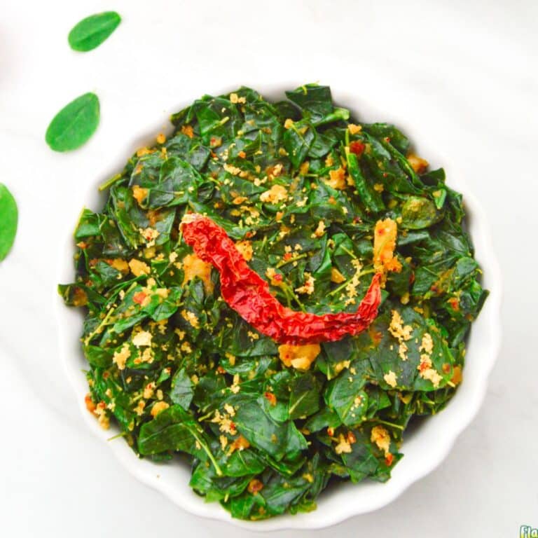 close up shot of moringa leaves curry in a white bowl with dry red chilli on top.