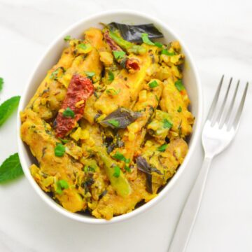 paneer majestic in a white bowl on a marble along with a fork, coriander and a lime wedge.