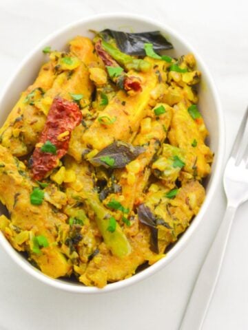 close up shot of paneer majestic in a white bowl on white table with fork and oriander leaves on side.