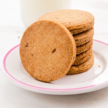 close up image of stack of jeera biscuits with one on the side in a white plate.