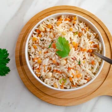 close up shot of carrot rice in white bowl with a spoon on wooden board.