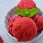close up shot of scoops of strawberry frozen yogurt with mint leaves on top in a white bowl on marble.