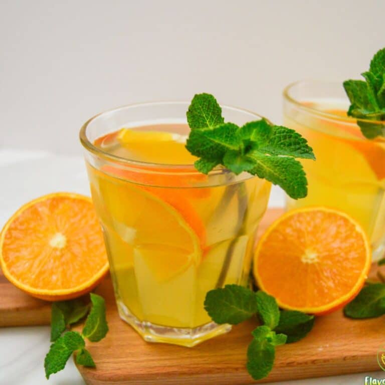 2 glasses of orange simple syrup placed on a wooden board with half cut orange and mint leaves.