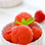 scoops of strawberry frozen yogurt with mint leaves on top in a white bowl.